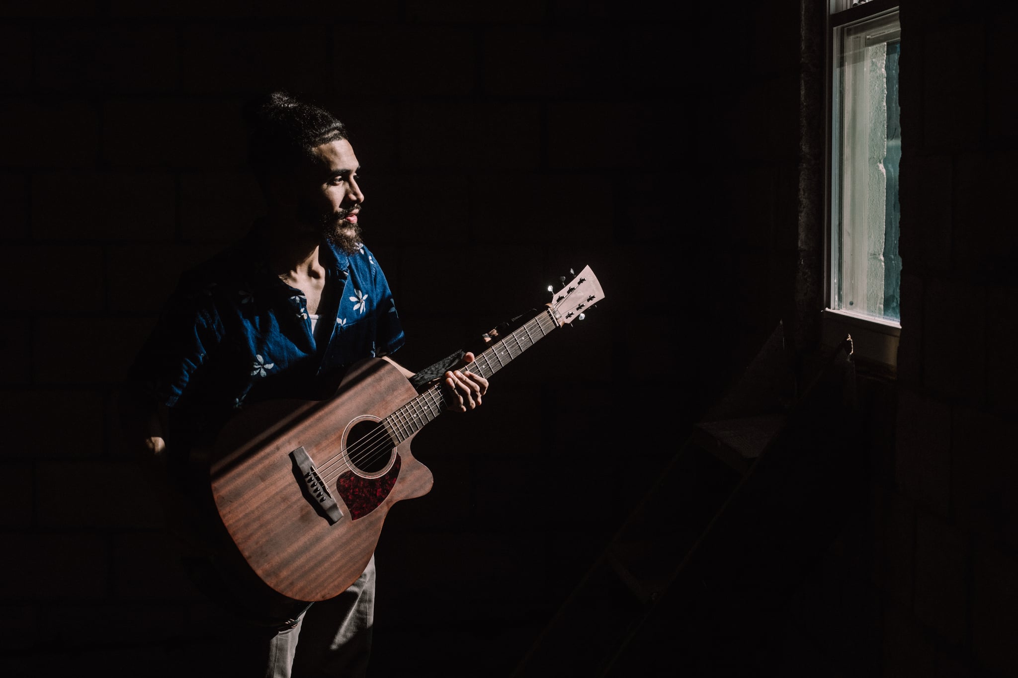 Cesar Cruz playing acoustic guitar in low window light